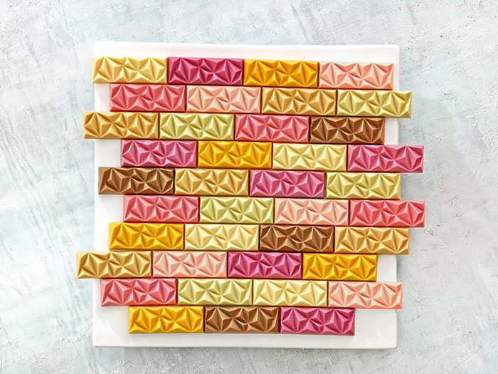 Multicolored confectionary bars sit in a brick pattern on a white wooden background. 