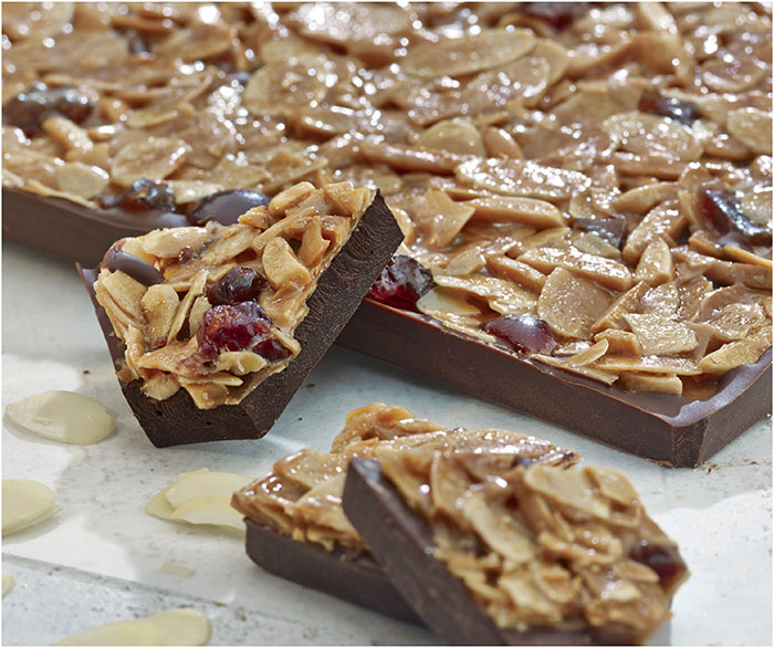 Bienetta florentine bark sits on a counter top covered in shaved almonds and cranberry. 
