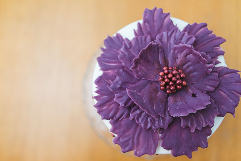 A large purple flower made of chocolate sits on a white platform, seen from a birds-eye view. 